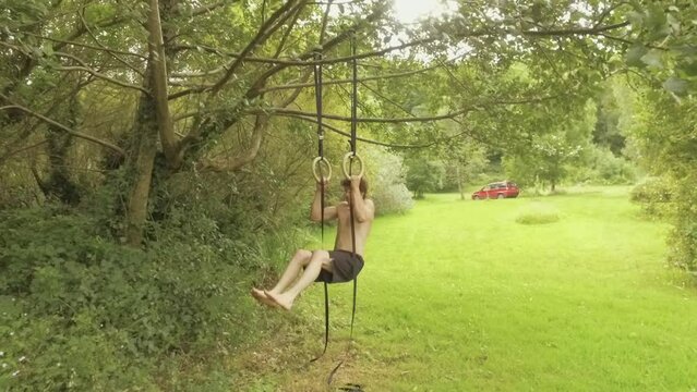Athletic young man doing ring pullups in garden
