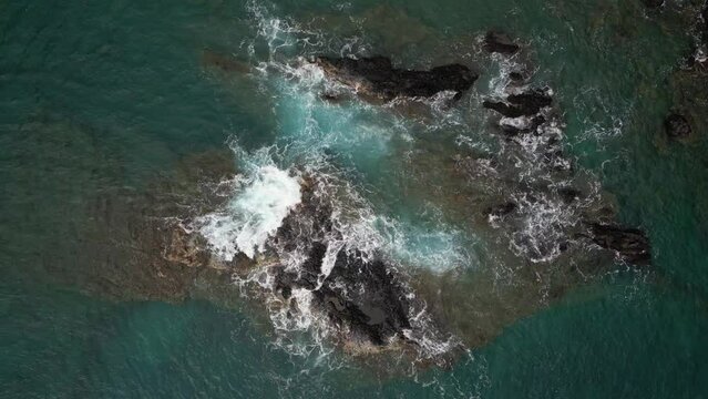 Aerial Top Down Over Waves Crashing Over Rocks. Slow Descending Spinning Shot