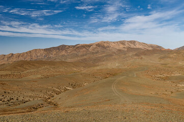 Eine unbefestigte Straße durch ein Hochland in der Mongolei mit einer Bergkette im Hintergrund