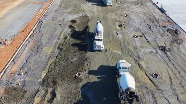 A massive line of concrete trucks drives past each other at a construction site.