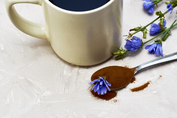Obraz na płótnie Canvas a mug with a drink of chicory chicory flowers and a spoon with powder and a chicory flower on the table