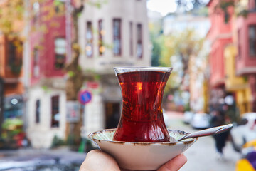 Turkish famous tea in a traditional cup in the hands of a person. City streets, city cafe.
