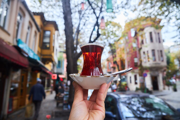 Turkish famous tea in a traditional cup in the hands of a person. City streets, city cafe.