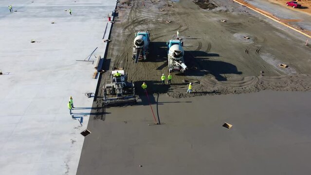 A screed machine smooths concrete while a supervisor observes.