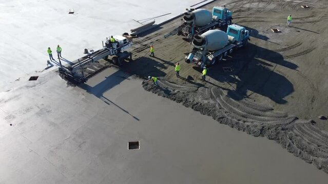 a concrete mixing truck uses the last of its concrete while a screed smooths out the concrete.