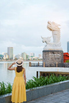 Woman Traveler with yellow dress visiting in Da Nang. Tourist sightseeing the river view with Carp Dragon Statue or Ca Chep Hoa Rong.Landmark and popular. Vietnam and Southeast Asia travel concept