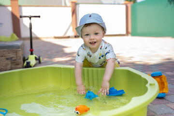 A boy in a hat plays with water in the yard in summer