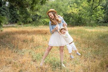 mother plays with her son in a meadow in the summer in straw hats