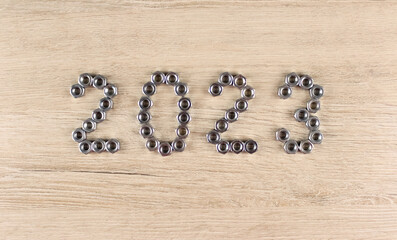 Number 2023 by metal nuts on a light wooden background. 2023 year