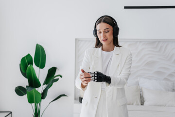 Attractive brunette girl in white suit uses touchpad on artificial hand adjusts arm functions....