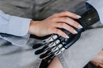 Cropped image of bionic hand prosthesis touching by second hand. Close up of hi tech artificial...