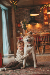 Obraz na płótnie Canvas Candid authentic happy little boy in knitted beige sweater hugs dog with bow tie at home on Xmas