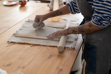 Busy artisan at work: pottery tattooed artist female working with raw clay in workshop. Young woman relax working with clay in studio. Concentrated sculptor making tableware. Hobby and leisure concept