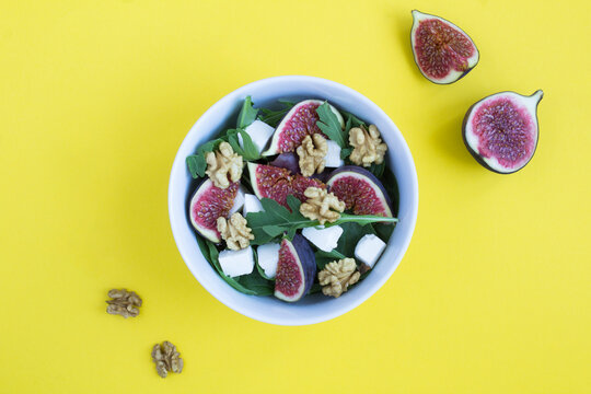 Salad with arugula, feta cheese, figs and walnuts in the white bowl on the yellow background. Top view. Copy space.