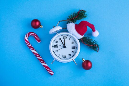 White alarm clock with Christmas Santa hat on the blue background. Top view. Copy space.