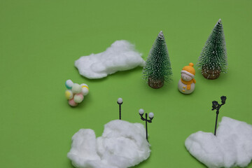 Winter idyll with pine trees, snow, street lights, Snowman with a yellow hat and scarf, colorful snowballs on a green background. Minimal winter conception.