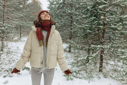 Delighted woman in outerwear enjoying snowy weather in winter forest 