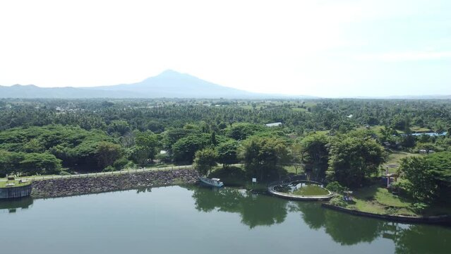 Aerial view of a serene reservoir with pine trees and the majestic Seulawah Agam volcano in the distance