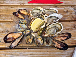 Many fresh opened oysters with lemon on a glass plate on dark wooden table.