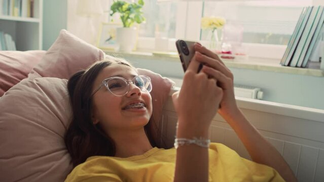 Caucasian teenage girl having video call while lying on back in her bed. Shot with RED helium camera in 8K.   
