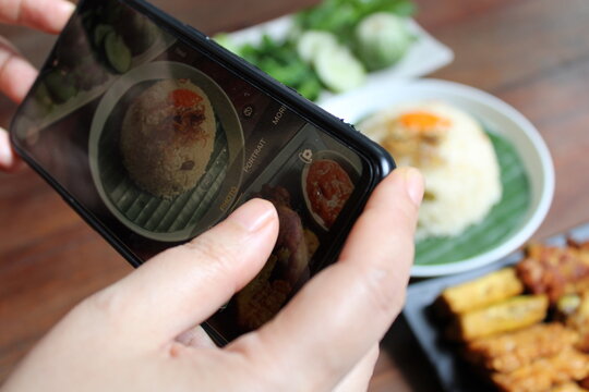 Woman hands takes photo of Indonesian traditional food Nasi Liwet on the table with phone