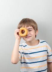 The blond boy looks through the donut as if through a monocle. Portrait on a light background.