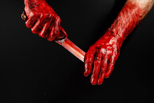 A man wipes a bloody knife with his hand on a black background. 