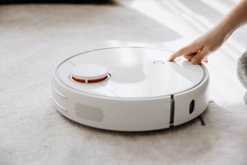 Child hand turn on smart robot vacuum cleaner. Modern smart device cleaning floor and carpet. Kid using wireless technology.