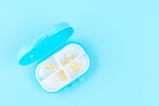 Plastic case with vitamin D capsules on a blue background close-up.