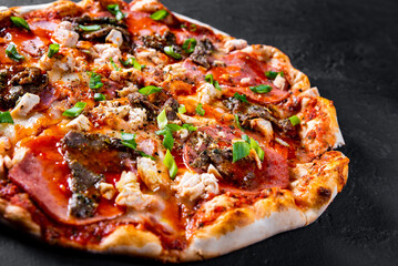 Pizza with Mozzarella cheese, salami, chicken meat, beef, ham, Tomato sauce, pepper, spices. Italian pizza on Dark grey black slate background
