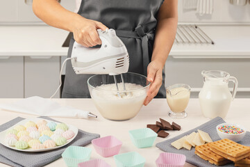 A hand mixer in the hands of a woman in an apron whips cream, mousse, ice cream. Making dessert in...