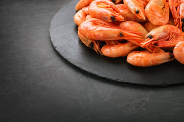 A lot of boiled shrimp in a shell on a black slate round board on a black background. Close-up. Perfect retouching. Copy space. Top and side view. Photos for menus, advertisements.