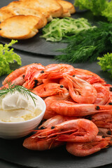 A lot of boiled shrimp on a black slate plate next to cottage cheese, bread, lettuce leaves, dill and fresh cucumber. Vertical photo for the menu. Bruschetta recipe. Top and side view.