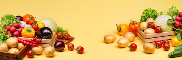 Lots of different fresh vegetables on a yellow background in wooden boxes. Potatoes, cabbage, radishes, lettuce, peppers, cucumbers, tomatoes. Copy space. Horizontal photo.Side view.