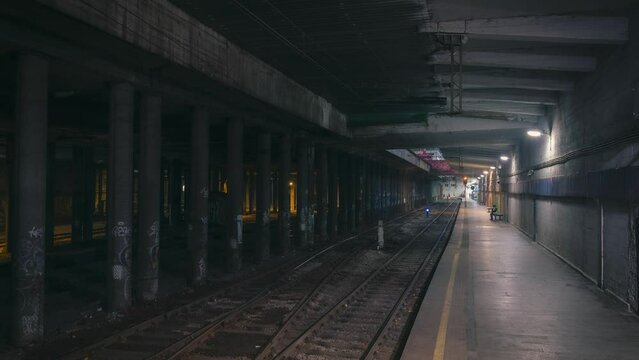 Time-lapse photography of abandoned railway / subway platform. Ghetto. Rainy autumn foggy weather in the night city. Gotham mood. Cinematic style. Dungeon columns and dim light. Graffiti on the walls.