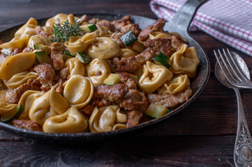Tortellini with turkey breast strips,  zucchini and cream sauce in a rustic iron pan on wooden table