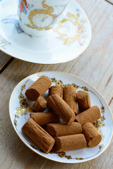 Tasty chocolate cookies are on the white plate on the wooden background with a white cup. Brown biscuits in the morning on the wooden table