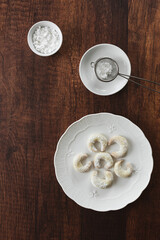 Draufsicht auf selbstgemachte Vanillekipferl auf einem weißen Teller und Puderzucker in einer Schüssel. Rustikaler brauner Holz Tisch.