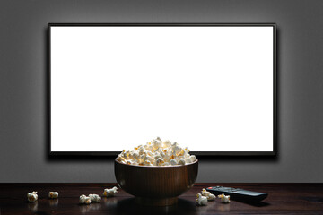 Television on a gray wall with remote control and popcorn bowl on the table. TV 4K flat screen lcd...