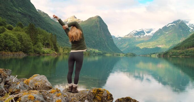 Lake, mountains and stretching woman hiking in nature for peace, freedom and fresh air while on adventure journey. Rain, river and back of girl trekking for health, wellness or Norway travel tour