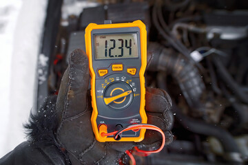 Mechanic test car electric system with multimeter, check car battery voltage. Man with voltmeter...