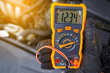 Checking car battery voltage. Mechanic check up car electric system with multimeter in cold winter conditions. Man with voltmeter measuring voltage level in car battery. Testing battery health - obrazy, fototapety, plakaty