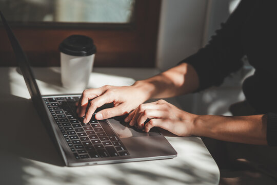 Crop picture of hand woman typing keyboard on laptop lighting sitting at cafe. Freelance business woman sitting in a coffee shop and video call conference or seacrh job or browse internet on laptop.