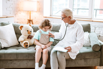 cute little curly haired girl plays doctor with a stethoscope and treats and cares a teddy bear on...