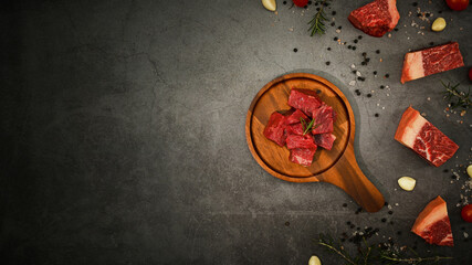 Raw picanha or rump beef meat chopped in cubes with pepper, sea salt and rosemary on black stone background