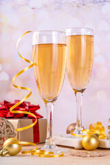Champagne for New Year party. Noel, Christmas, New year greeting card background with two champagne glasses, gift box and holiday decoration, on bokeh golden background copy space