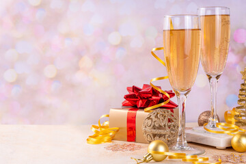 Champagne for New Year party. Noel, Christmas, New year greeting card background with two champagne glasses, gift box and holiday decoration, on bokeh golden background copy space