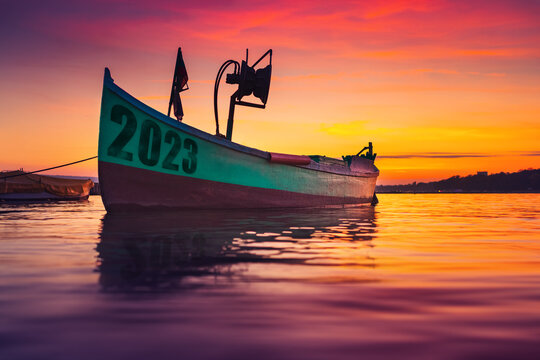 2023 New Year Concept. Fishing Boat On Shore And Ripple Sea Water On Dramatic Colorful Sunset