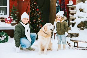 siblings girl sister and teenage cute boy brother in knitted sweater and hat having fun with first snow and cute pet dog labrador at porch of country house, concept of winter spirit and Christmas