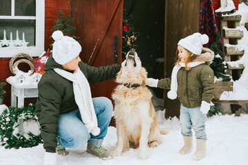 siblings girl sister and teenage cute boy brother in knitted sweater and hat having fun with first snow and cute pet dog labrador at porch of country house, concept of winter spirit and Christmas